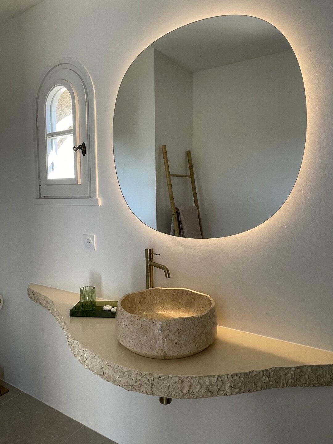 Badezimmer mit Natursteinwaschbecken und rundem beleuchteten Spiegel