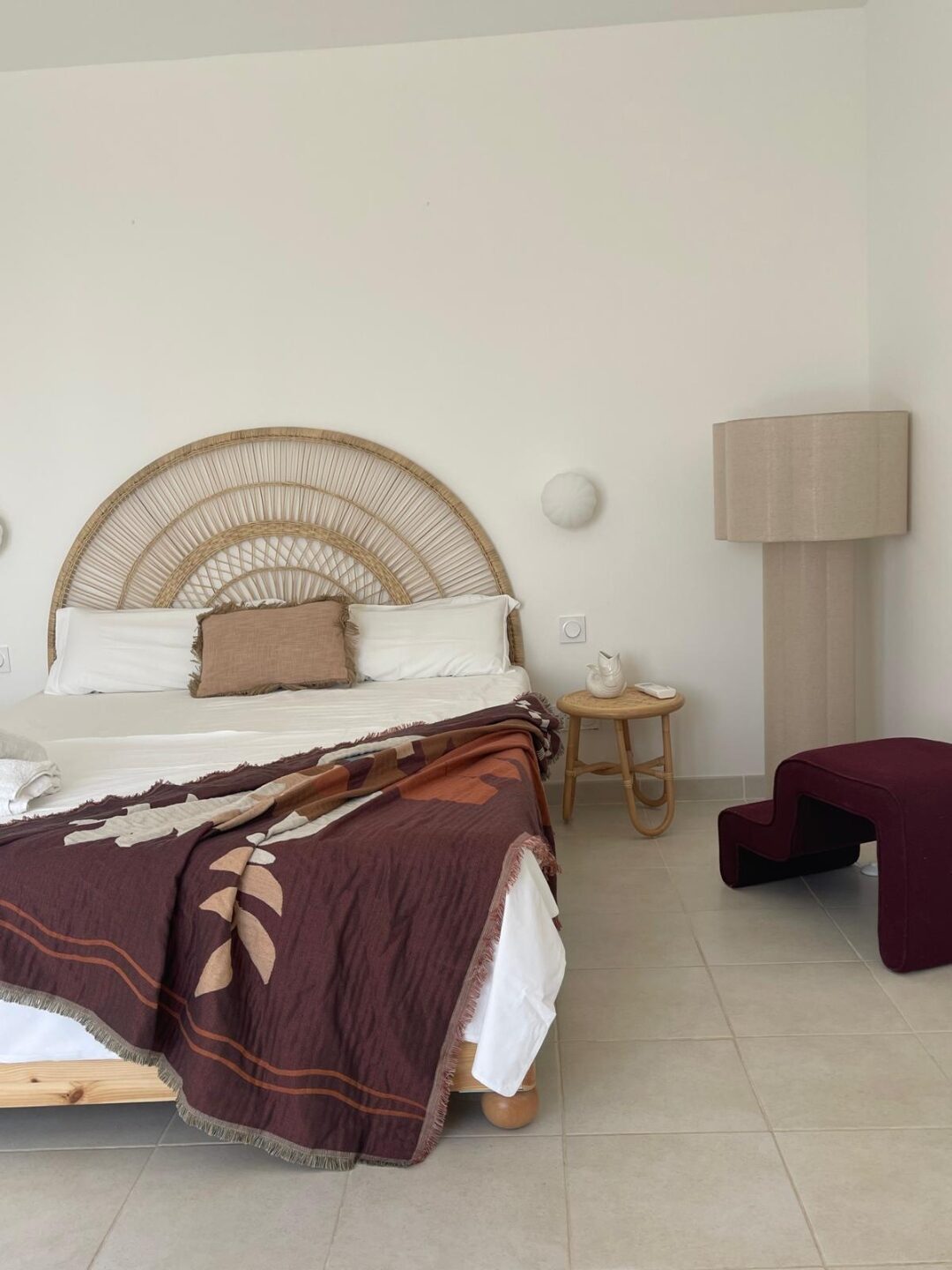 Schlafzimmer mit rundem Rattan-Kopfteil und Bordeaux-Plaid